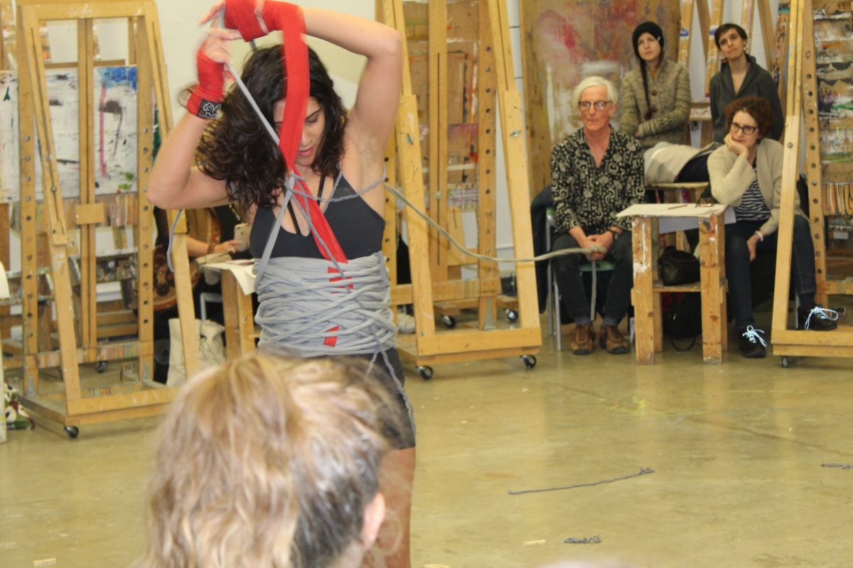 image of a woman wrapped in thick ropes and with hands in red tape dancing for an audience