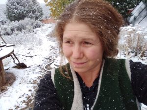 A photo of a white red headed woman named Riveral Sun. She is outside. There is snow in the background.