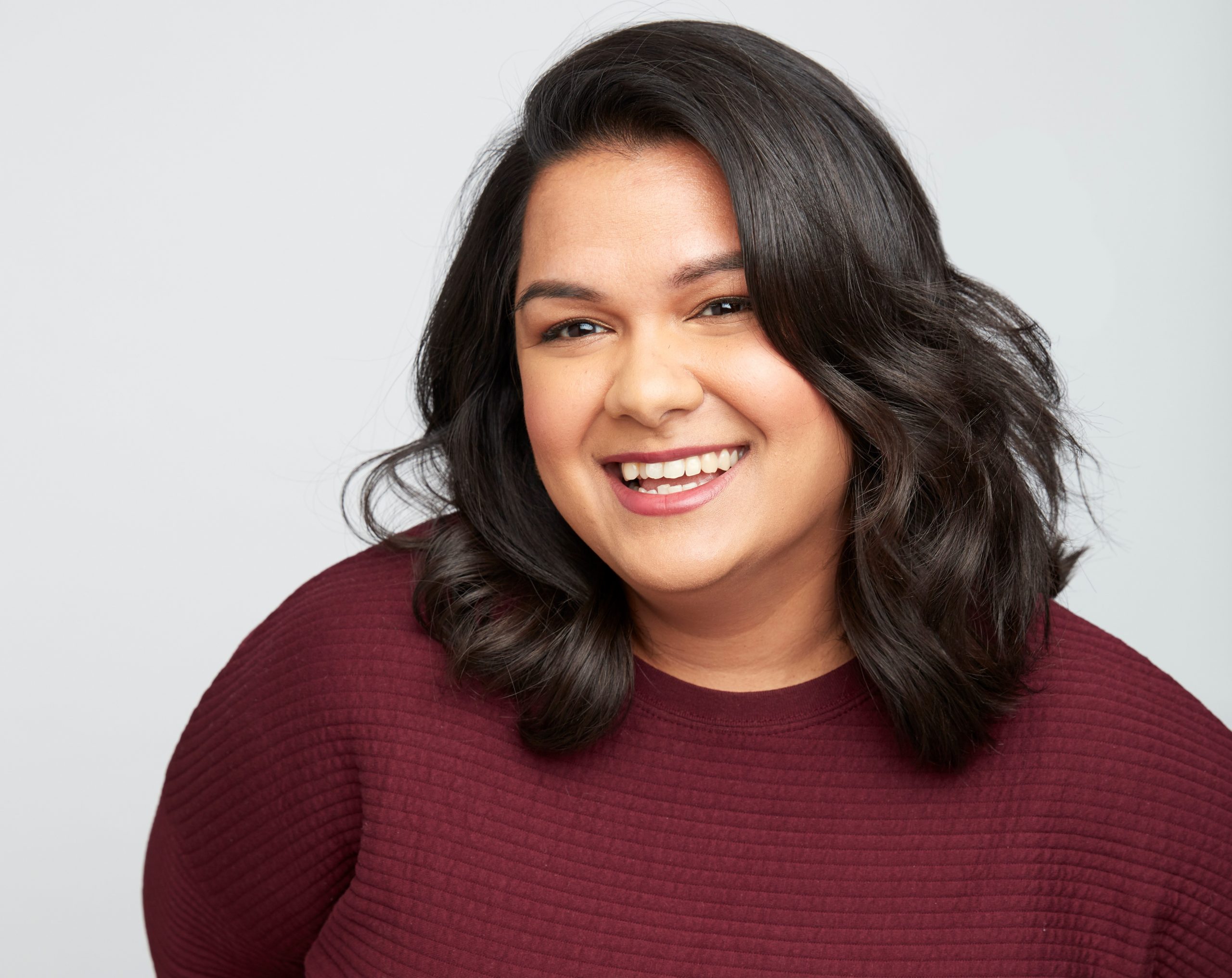 An image of a young woman with long brown-black wearing a maroon scoop neck sweater.