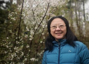 Photo of asian woman in a blue puffer coat with spring cherry blossoms in the background
