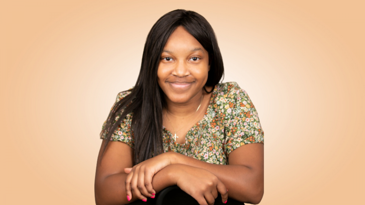 An image of a young black woman, wearing a flowered dress, hands folded in front of her.