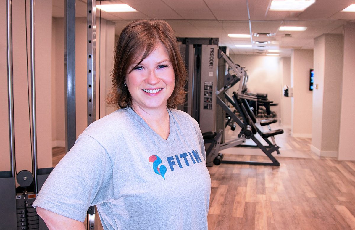 An image of a white woman at a gym wearing a tshirt that reads "fit in".