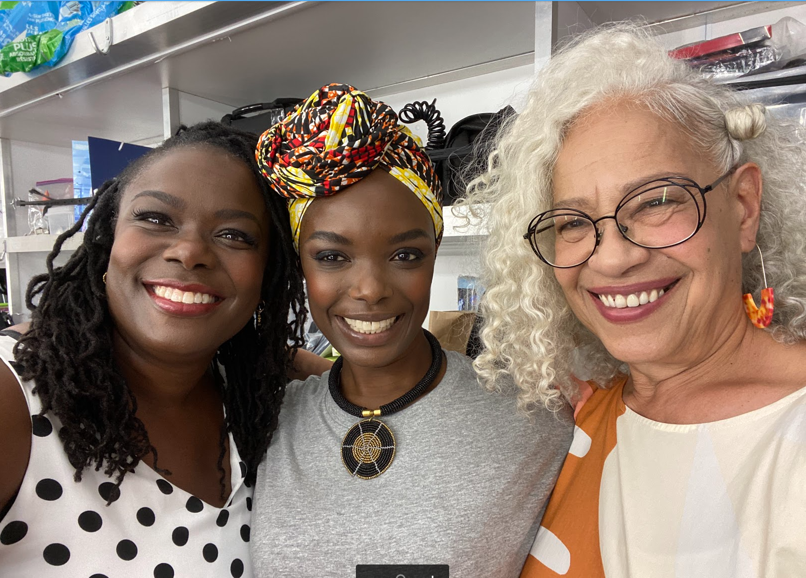 Image of two black women and one grey haired woman of colour, standing, arms across each others shoulders in unity.