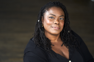 Head shot of a black woman with long black braids, wearing blue shirt.
